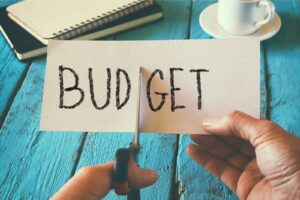 Image of a hand holding a pair of scissors over a paper with the word 'budget' written on it.