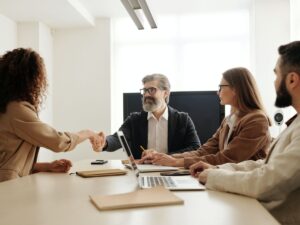 Four business professionals in a meeting, with two shaking hands in agreement over employment opportunities.